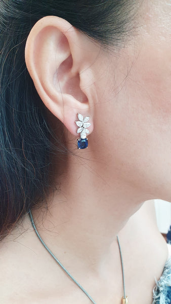Close-up of an ear wearing a floral earring with a blue sapphire.